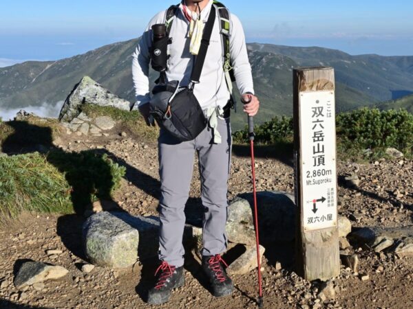 カメラバッグを肩から斜め掛けにして登山をしている画像